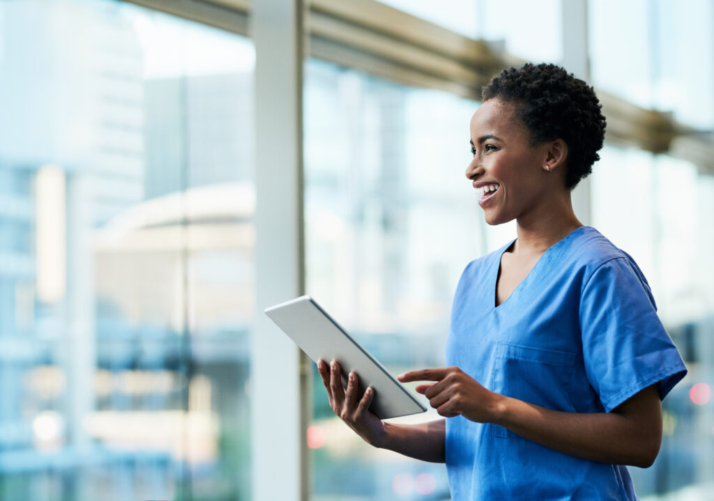 A person in scrubs using a digital tablet looking out a glass window